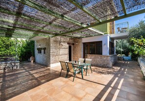 A patio with a table and chairs, a stone wall, and a covered area with a pergola. - Villa Maistro in Lefkada (Lefkada)