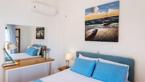 A hotel room with a bed, a desk, a mirror, and a painting of a beach scene. - Villa Pelagos Kyma in Lefkada (Lefkada)