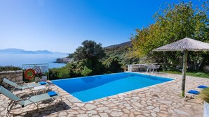 A swimming pool with stone flooring, lounge chairs, and a view of the sea. - Villa Pelagos Kyma in Lefkada (Lefkada)