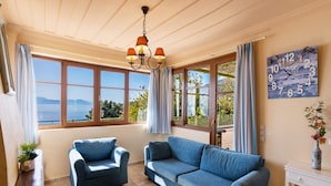 A living room with a sofa, armchair, and a table with a teapot and cups. - Villa Pelagos Kyma in Lefkada (Lefkada)