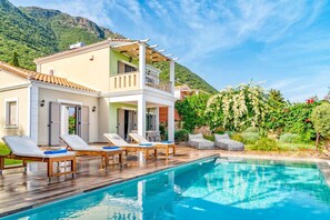 A two-story building with a pool, lounge chairs, and a mountainous backdrop. - Villa Melanthi in Lefkada (Lefkada)