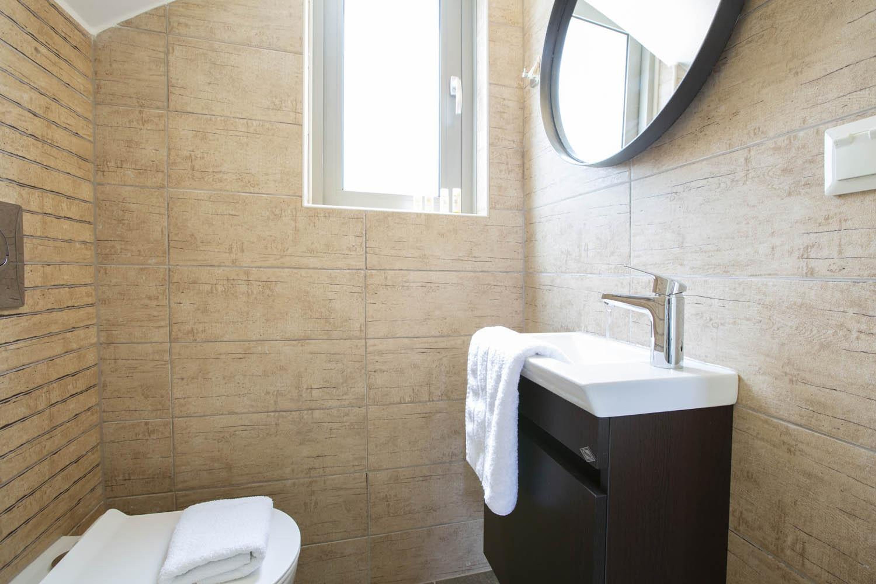 A bathroom with a wooden wall, a white sink, a mirror, and a window.
