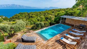Uma área de piscina com deck de madeira, espreguiçadeiras e um muro de pedra.