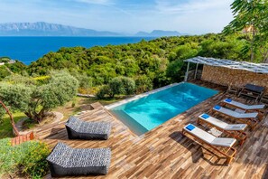 Ein Poolbereich mit Holzterrasse, Liegestühlen und einer Steinwand.