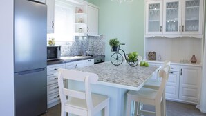 A kitchen with white cabinets, a stainless steel refrigerator, a marble countertop, and a dining area with white chairs. - Villa Melanthi in Lefkada (Lefkada)