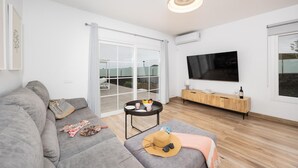 A modern living room with a grey sofa, a small round table with a bowl of fruit, a television, and a wooden cabinet. - Villa Yaiza Secret 1 (Yaiza)