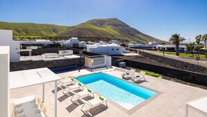 A pool area with lounge chairs, a table with chairs, and a view of a mountain. - Villa Yaiza Secret 1 (Yaiza)