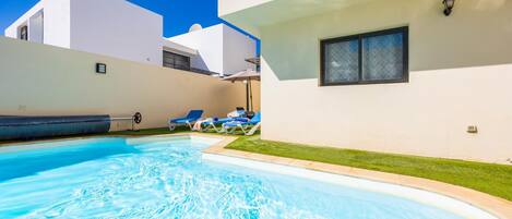 A swimming pool with lounge chairs, a water slide, and a white building with a window.