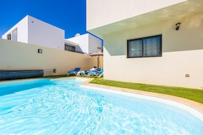 Piscina com espreguiçadeiras, tobogã e um prédio branco com janela.