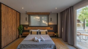 A modern bedroom with a large bed, wooden headboard, and a view of the outdoors. - Villa Omega in Alonnisos (West Mani)