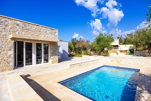 Ein Steinhaus mit Swimmingpool, blauem Himmel und umgebender Grünfläche.