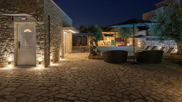 A stone building with a door, outdoor seating area with umbrellas, and a stone-tiled patio. - Villa Omega in Alonnisos (West Mani)