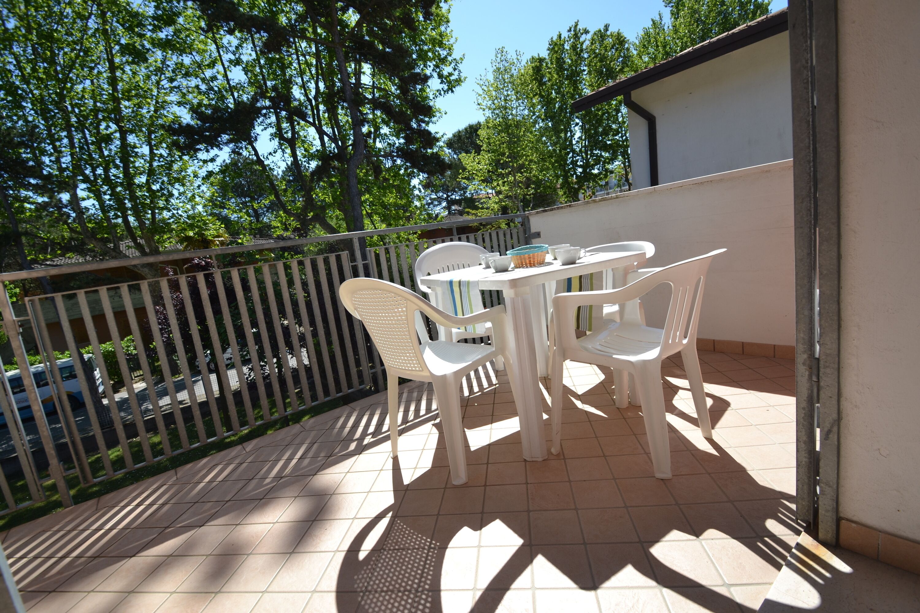 Ein Balkon mit Tisch und Stühlen, einem Geländer und Blick auf Bäume und parkende Autos.