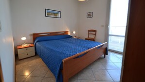 Ein Schlafzimmer mit einem Bett, Nachttischen, einem Sessel und einem Fenster mit Jalousien.
