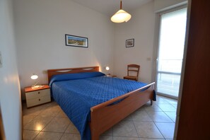Ein Schlafzimmer mit einem Bett, Nachttischen, einem Sessel und einem Fenster mit Jalousien.