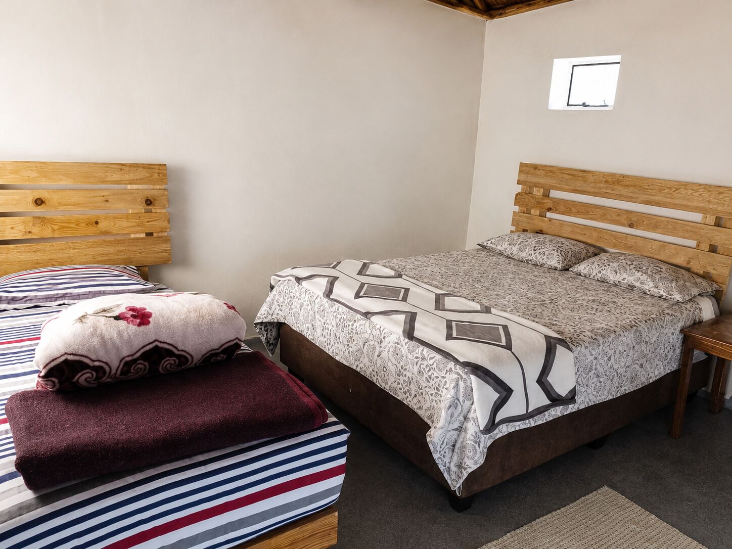 Un dormitorio con una cama de madera, un cojín a rayas, un cojín floral y una colcha estampada.