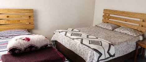 Un dormitorio con una cama de madera, un cojín a rayas, un cojín floral y una colcha estampada.
