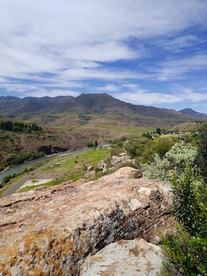 A mountainous landscape with a river, rocky foreground, and distant buildings.