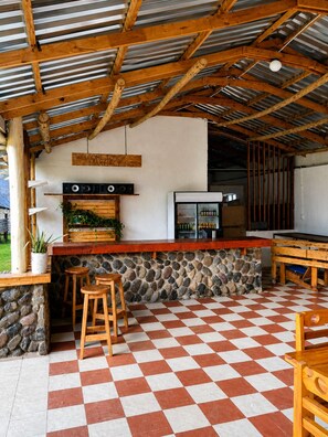 A rustic outdoor kitchen area with a stone wall, wooden stools, and a checkered floor.