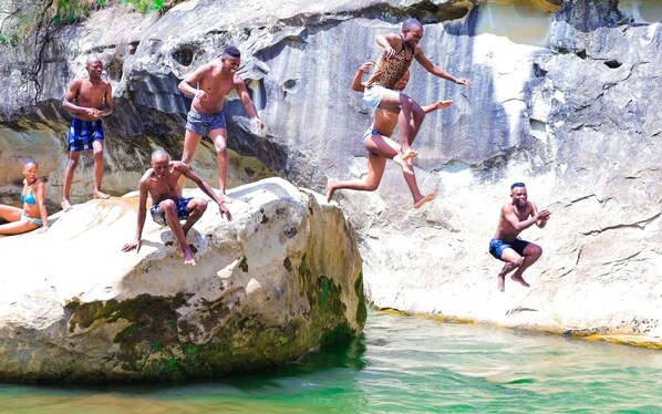 People jumping off a rock into a pool.