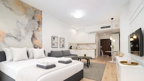 A modern bedroom with a large bed, a sofa, a dining area, and a kitchen. - MARGI Milky Apartament (Szczecin)