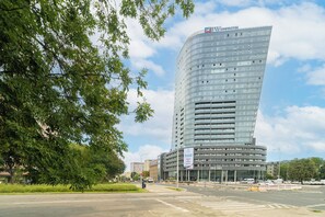 A modern high-rise building with a curved facade, likely a hotel or office building, with a clear sky and some greenery in the foreground.
