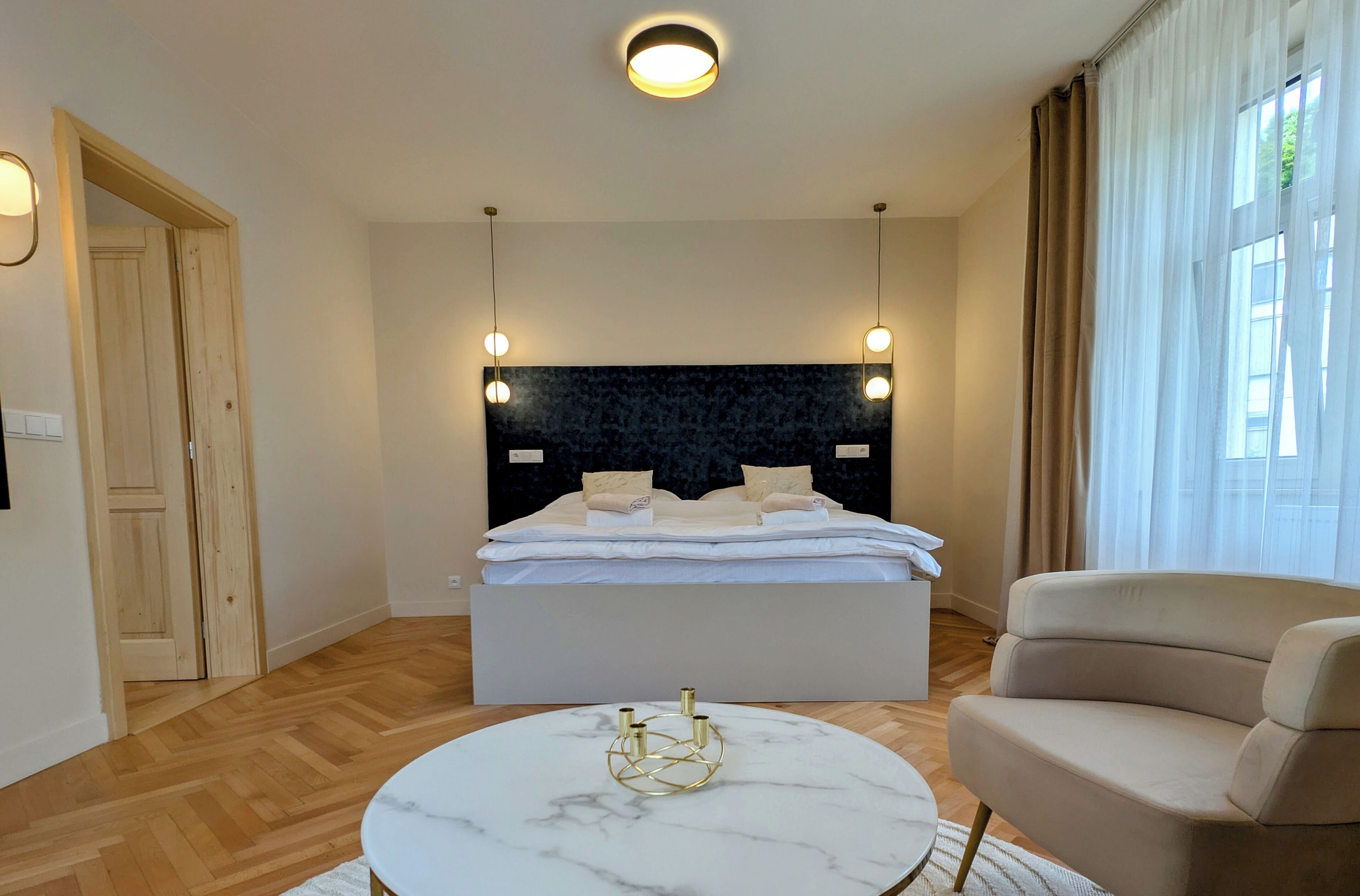 A bedroom with a bed, bedside lamps, a round table, and a sofa.