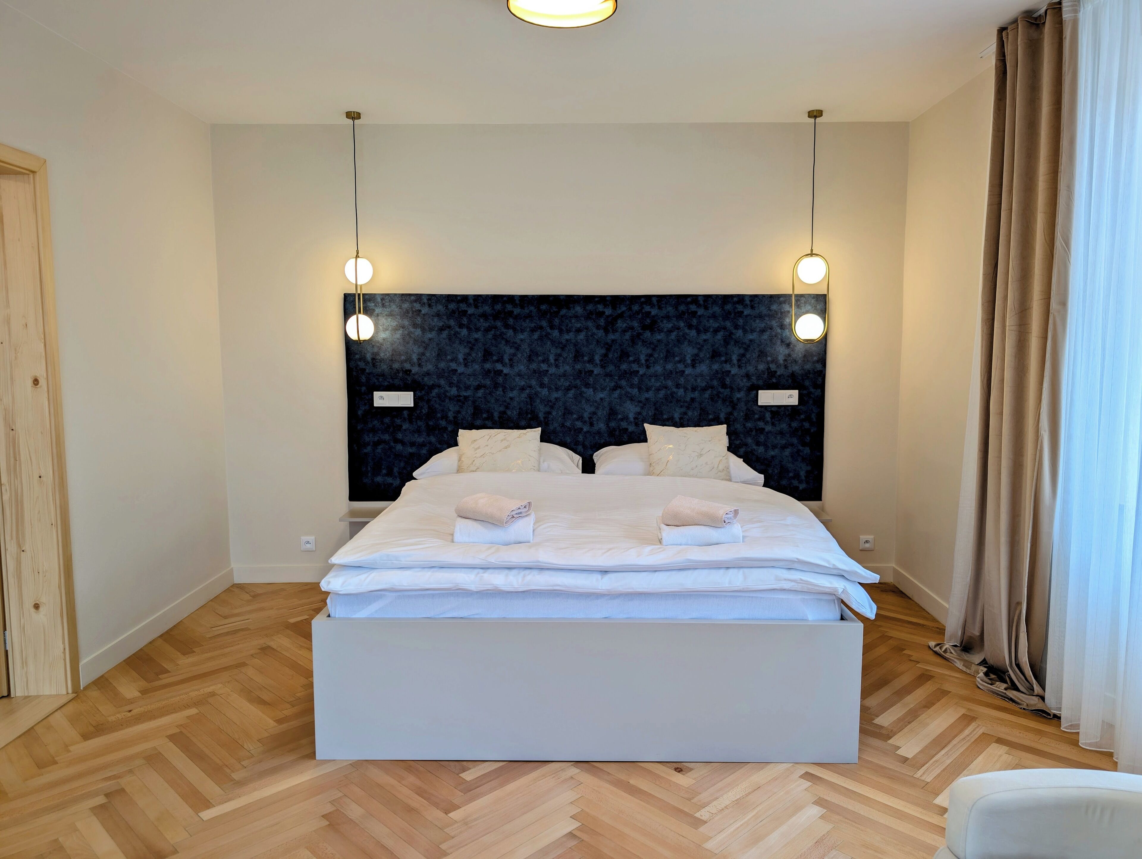 A hotel room with a large bed, two bedside tables, a dark headboard, and two pendant lights.