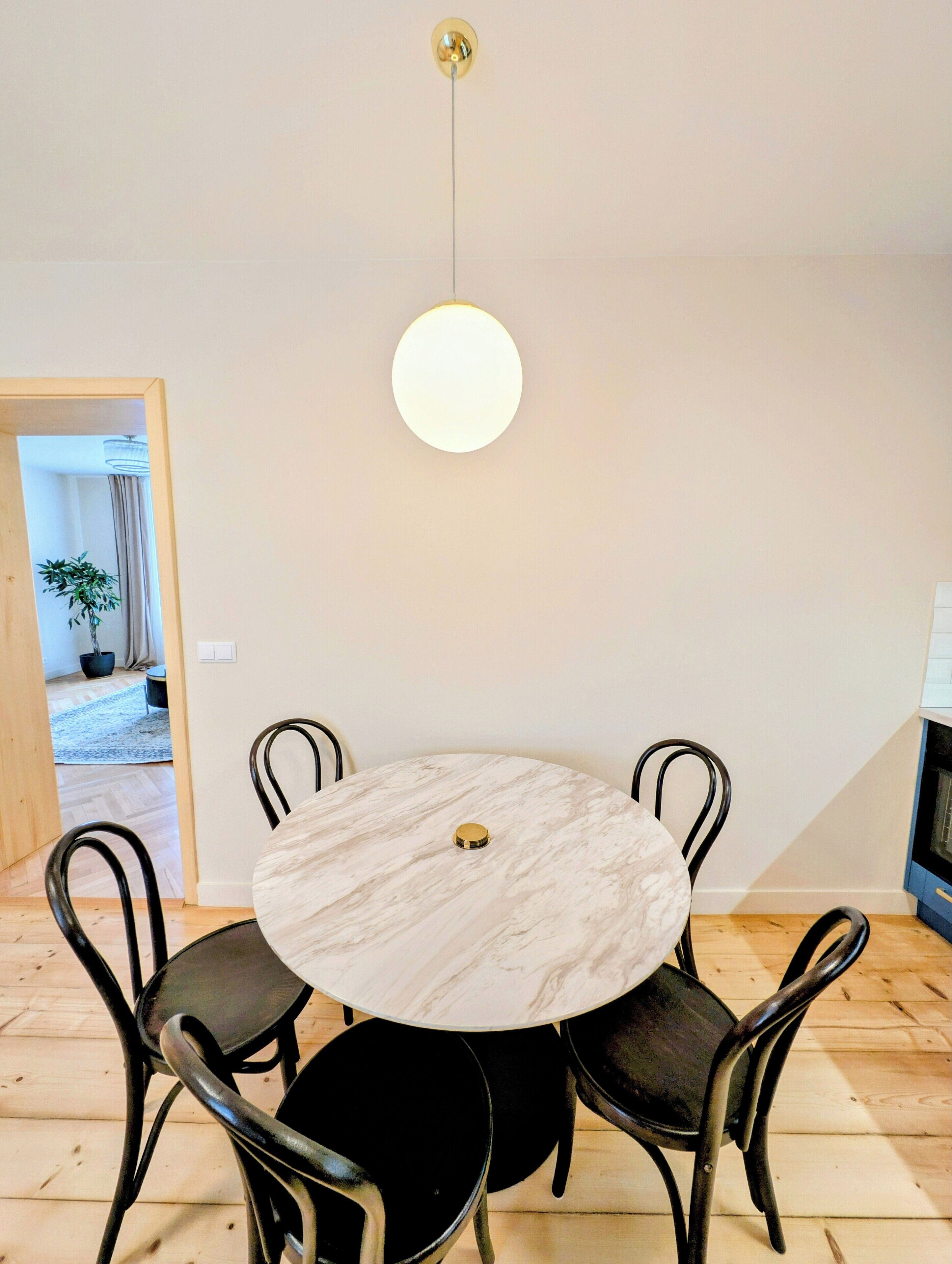 A round dining table with a marble top, surrounded by four black chairs, in a room with wooden flooring and a white wall.