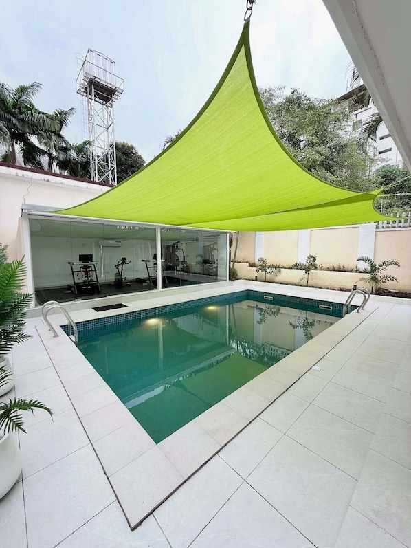 A swimming pool with a covered patio area, a glass enclosure, and a metal structure in the background. - Goldvika  (Abuja)