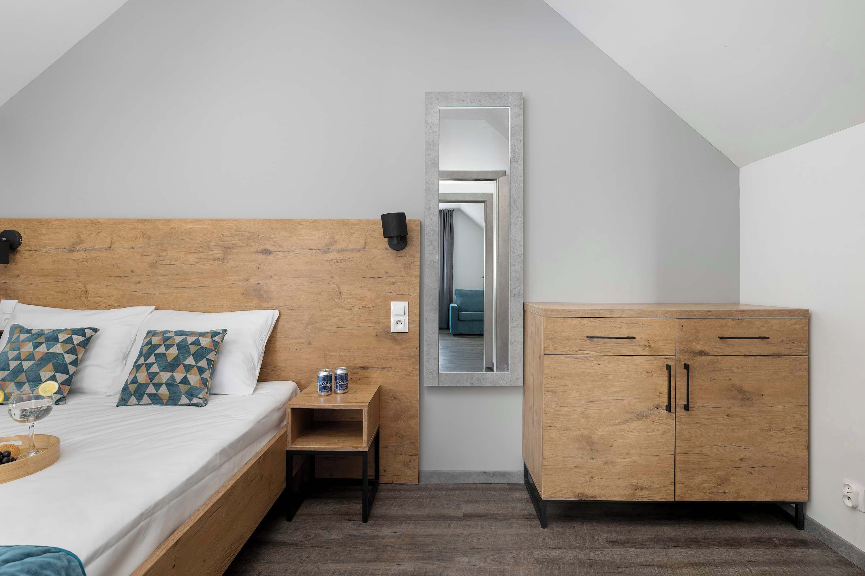 Une chambre à coucher avec une tête de lit en bois, un lit recouvert de draps blancs, une petite table de chevet avec une lampe, une armoire et un miroir au mur.