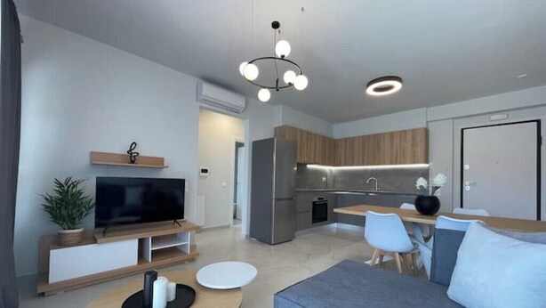 Een moderne woonkamer met een flatscreen televisie, een ronde salontafel, een bank en een eethoek met stoelen.