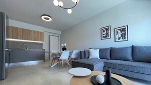 Een moderne woonkamer met een grijze bank, een ronde salontafel en een keuken op de achtergrond.