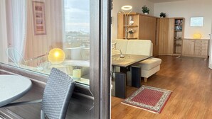 Een moderne woonkamer met een glazen eethoek, een bank, houten kasten en een rood vloerkleed met een patroon.