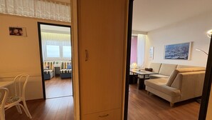 Een kamer met een houten vloer, een witte stoel, een bank, een tafel en een raam met gordijnen.