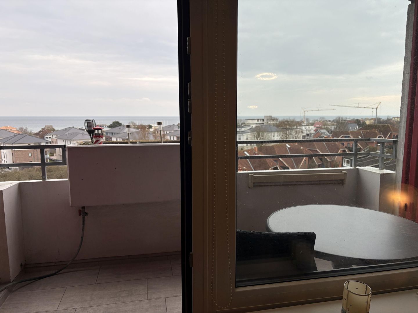 Un balcón con una mesa y una silla, vista al mar y un paisaje urbano de fondo.