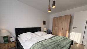 A bedroom with a bed, bedside lamps, a nightstand, a wardrobe, and a door. - Stranddistel 5 - "Stranddistel" vacation home with 5 residential units... (Dahme)
