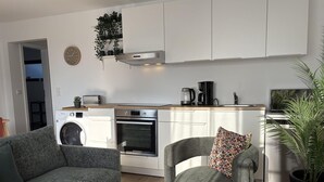A modern kitchen with a washing machine, oven, and coffee maker. There are two grey sofas and a small table. - Stranddistel 5 - "Stranddistel" vacation home with 5 residential units... (Dahme)