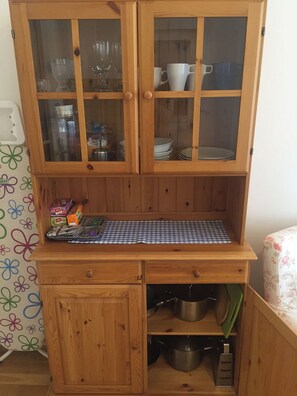Ein Küchenschrank aus Holz mit Glastüren, einer karierten Decke und Küchenutensilien.