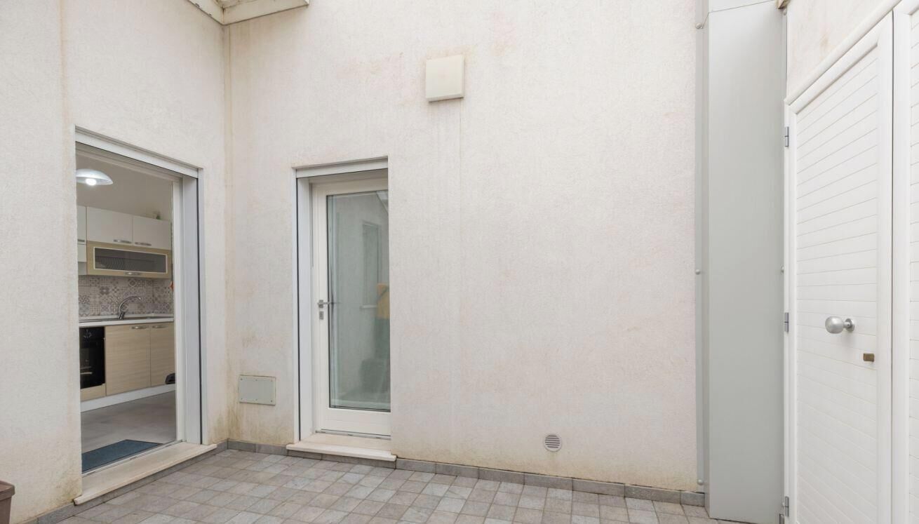 Un ambiente piccolo e chiuso con una porta, un pavimento piastrellato e una cucina a vista con pensili e un piano di lavoro.