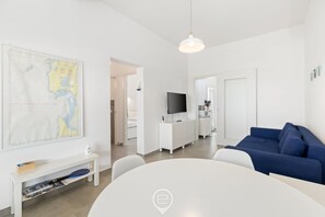 Ett modernt vardagsrum med ett vitt bord, en blå soffa och en platt-TV.
