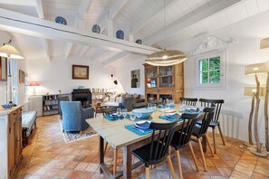 Een eethoek met een grote tafel gedekt voor zes personen, omringd door stoelen, met zicht op de keuken en woonkamer op de achtergrond.