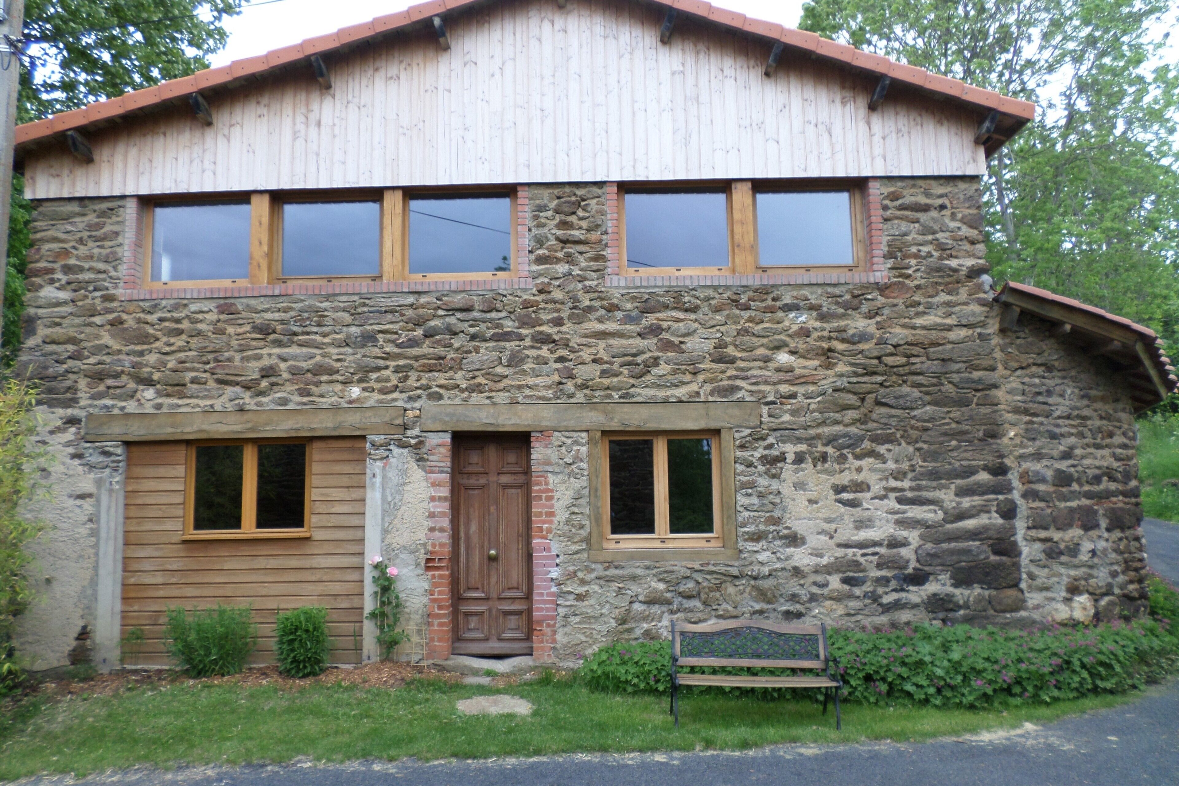 Un edificio de piedra con puerta principal de madera, dos ventanas y un banco en el exterior.
