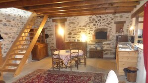Une pièce rustique avec une échelle en bois, une table ronde entourée de chaises, un tapis à motifs et une petite kitchenette.