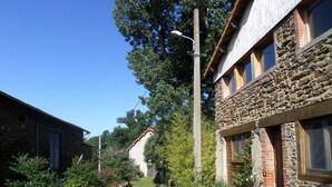 Un étroit sentier pavé mène à un bâtiment en pierre où se trouvent un banc en bois et un lampadaire.