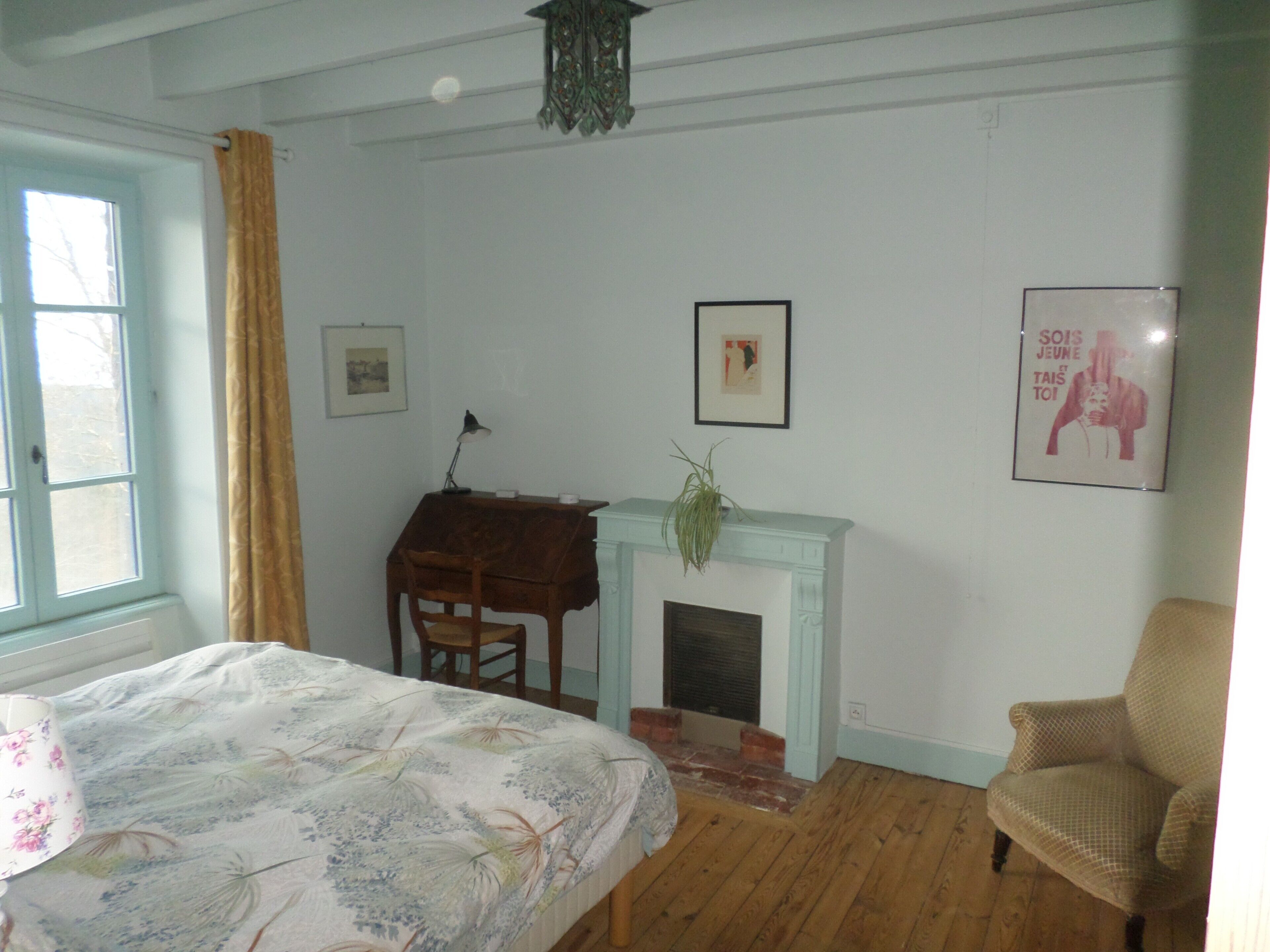 Een slaapkamer met een bed, een bureau, een stoel, een open haard en een raam met gordijnen.