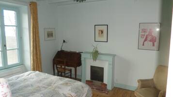 Een slaapkamer met een bed, een bureau, een stoel, een open haard en een raam met gordijnen.
