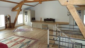 Ein geräumiges Loft mit hohen Decken, freiliegenden Holzbalken, einer Treppe und einem großen Fenster.