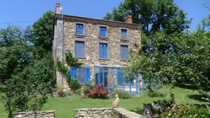 Ein Steinhaus mit blauen Fensterläden, ein Garten mit Blumen und eine Statue.