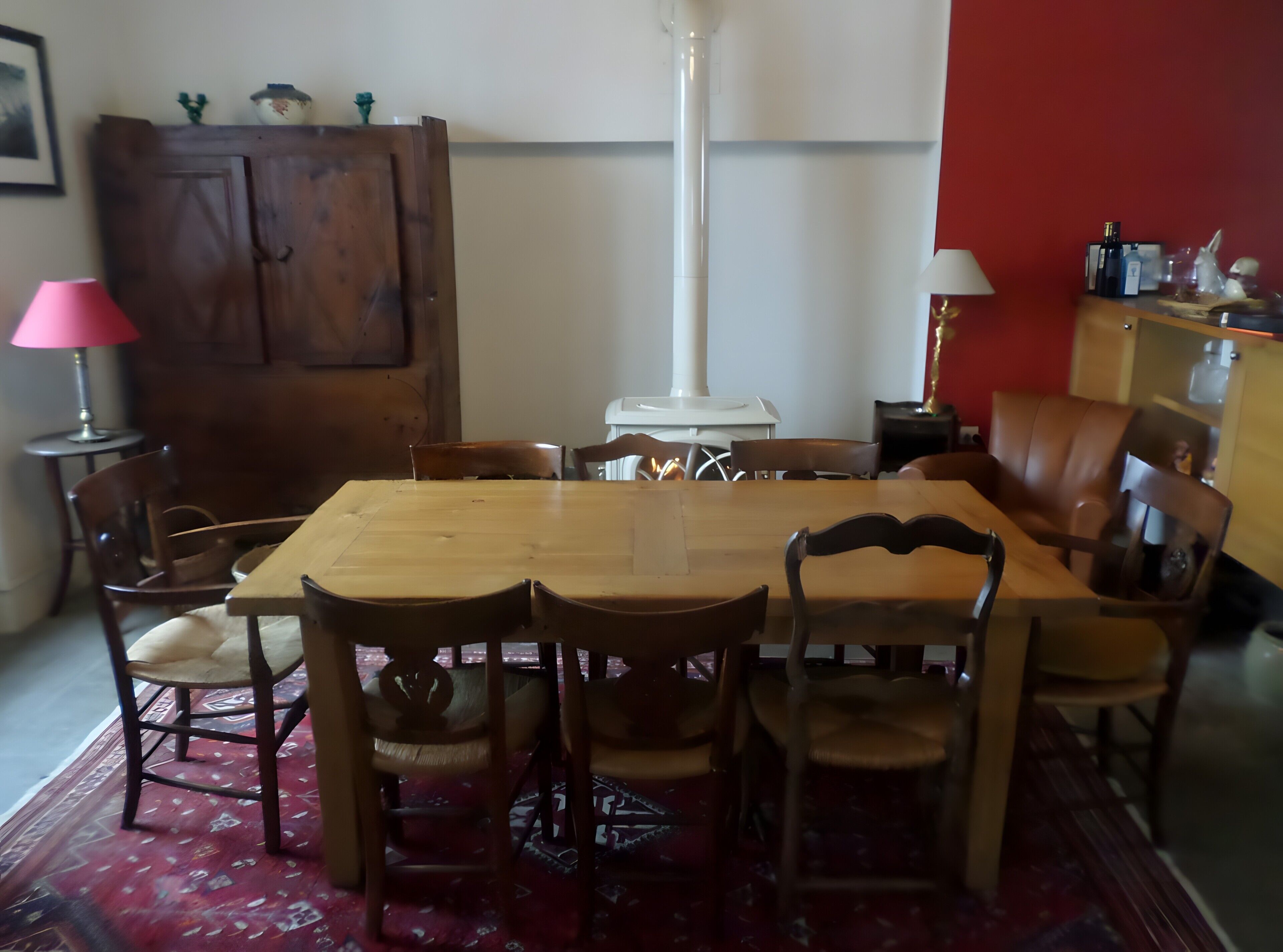 A dining area with a wooden table, chairs, a red carpet, a white lamp, and a cabinet.